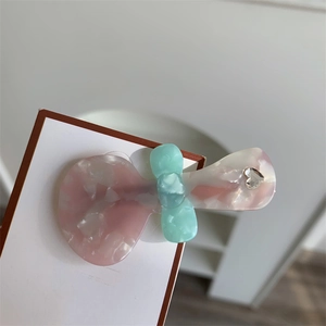 Dettaglio di un fermaglio per capelli in acetato a fiocco con trama marmorizzata rosa e verde