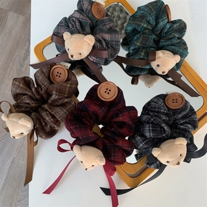 Detail of plaid scrunchies with plush bear, silk bow, and button on mirror surface