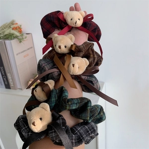 Detail of plaid scrunchies with teddy bear charms on a wrist in a cozy setting