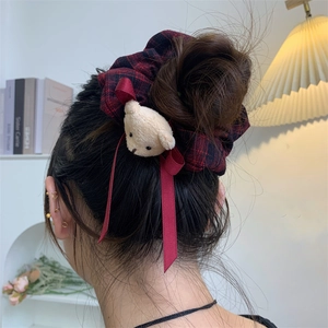 Red plaid hair scrunchie with plush bear charm and long ribbon on model's bun