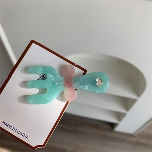 Dettaglio del fermaglio in resina verde marmo con fiocco rosa e strass a cuore su carta