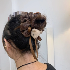 Close-up of brown plaid scrunchie with plush bear and bow on a messy bun hairstyle