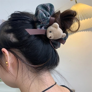 Close-up of a green plaid scrunchie with plush bear charm on a female hairstyle
