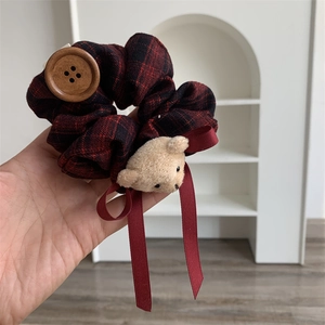Detail of red plaid scrunchie featuring a plush bear head and wooden button charm