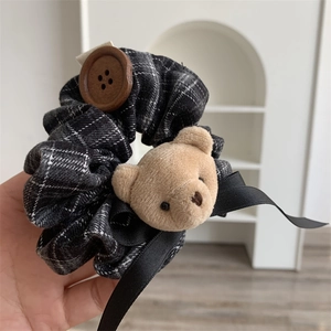 Detail of plaid scrunchie featuring a plush bear head and decorative wooden button