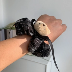 Close-up of black plaid scrunchie with teddy bear and ribbon on a wrist
