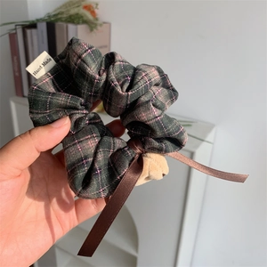 Detailed close-up of a green plaid scrunchie with a plush bear and satin bow detail