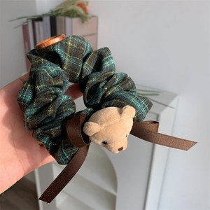 Detail of dark green plaid scrunchie featuring a cute plush bear and brown ribbons