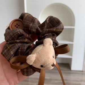 Detail of coffee plaid scrunchie featuring a plush bear head and wooden button charm