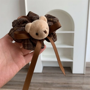 Detail of brown plaid scrunchie with plush bear head and decorative satin bow ribbon