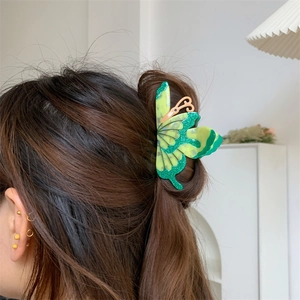 Detailed view of a green 3D butterfly hair claw clip worn in a half-up hairstyle