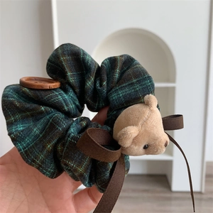 Close-up of a green plaid hair scrunchie with a plush bear, wooden button, and brown ribbon
