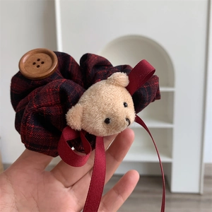 Detail of red plaid fabric scrunchie with cute teddy bear plush and wooden button