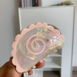 Close-up of a pink scalloped acetate hair claw clip with marble texture and small rhinestone