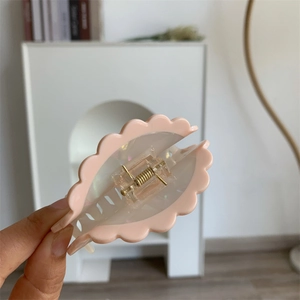 Macro shot of a light pink wave-edge acetate hair claw with golden metal spring details