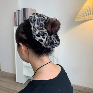 Detailed view of leopard print scrunchie worn on a bun hairstyle in warm indoor lighting