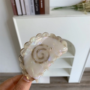 Detail view of the pearl white acetate hair claw with spiral pattern and small rhinestone