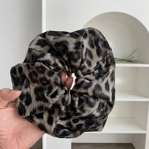 Handheld view of a large leopard print faux leather scrunchie with detailed pleats