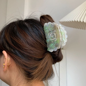 Detail of an iridescent acetate hair claw clip with shell petal design worn by a model