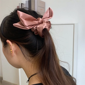 Pink satin bow scrunchie for women shown on a ponytail in a minimalist indoor setting