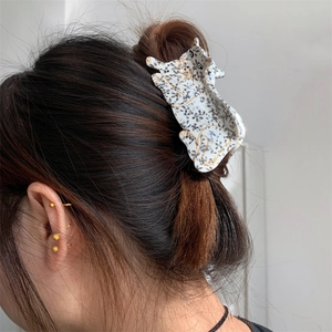 Detailed view of a white leopard acetate hair claw clip with black spots on brown hair