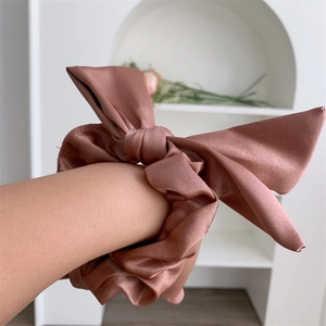 Macro view of a large rose gold satin bow scrunchie worn on a wrist for size reference