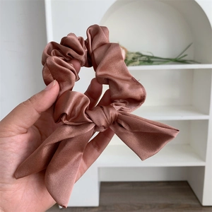 Detail of dusty rose satin scrunchie with bow decoration held against a clean background