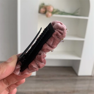 Détail macro d'une pince à cheveux en velours rose poudré avec strass et volants