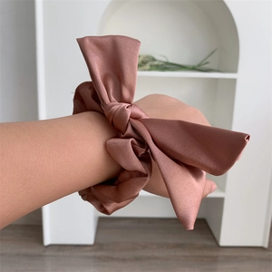 Detail of silk satin bow scrunchie in dark brown worn on wrist for a smooth texture