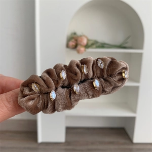 Détail d'une pince à cheveux en velours marron ornée de strass brillants sur fond doux