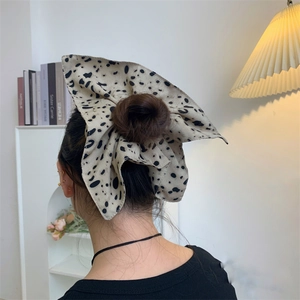 Detailed view of a cream polka dot bow hair scrunchie worn on a messy bun hairstyle