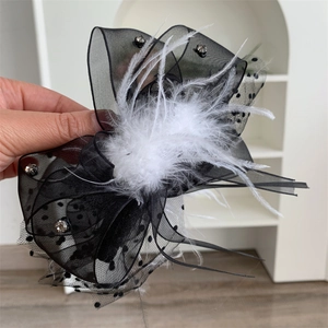 Close-up of black lace polka dot bow hair claw with white feathers and rhinestones