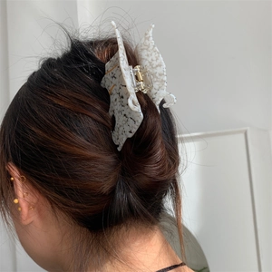 Gros plan détaillé d'une pince à cheveux papillon en acétate gris sur cheveux châtains
