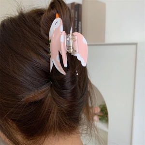 Détail d'une pince à cheveux en forme d'oiseau rose et blanc portée sur cheveux bruns