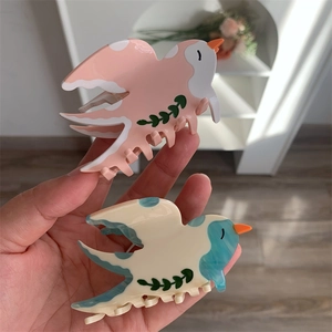 Vue détaillée des pinces à cheveux en acétate en forme d'oiseau rose et bleu