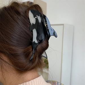 Orca-shaped acetate hair claw clip with rhinestones shown on brown hair for size reference