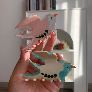 Détail de pinces à cheveux en acétate en forme d'oiseau rose et bleu avec motifs de feuilles
