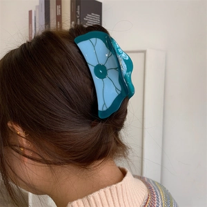 Vue macro d'une grande pince à cheveux en acétate avec motif floral contrasté vert et bleu