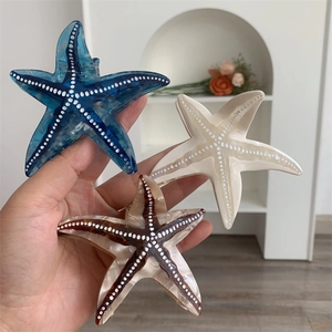 Vue détaillée des pinces à cheveux étoile de mer en acétate bleu, blanc crème et écaille