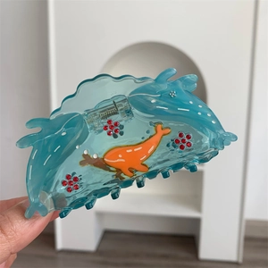 Detailed close-up of a blue whale-shaped acetate hair claw with red rhinestone flowers