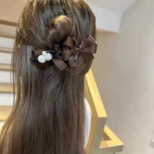 Detail showing dark brown silk bow hair clips with white pearls and metal pendant in hair