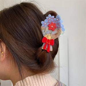 Dettaglio della pinza per capelli in acetato con fiori, strass e un fiocco rosso tra i capelli