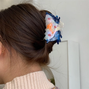 Detailed view of an acetate ocean-themed hair claw with blue fish and sparkling accents