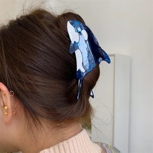 Detailed view of an orca-shaped acetate hair claw clip worn on long dark brown hair