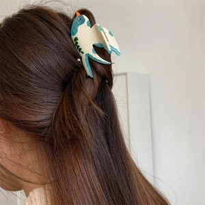 Détail d'une pince à cheveux en acétate en forme d'oiseau sur de longs cheveux bruns lisses