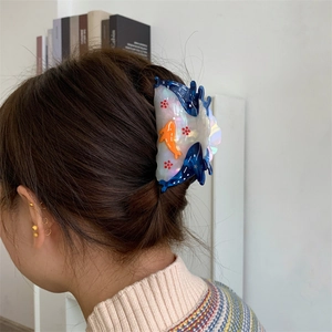 Detail view of a large acetate shark hair claw with ocean theme on a person's hairstyle