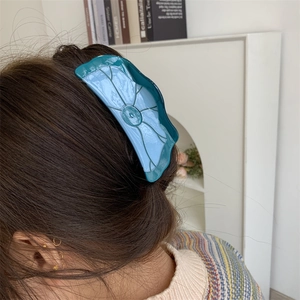 Détail d'une pince à cheveux en acétate vert en forme de lotus sur cheveux longs