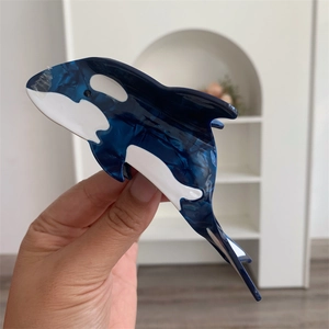 Detail shot of orca-shaped acetate hair claw clip with blue marble pattern and sleek design