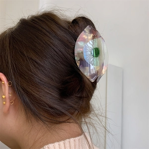 Gros plan d'une pince à cheveux en acétate en forme d'œil au fini irisé sur la tête