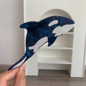 Detailed close-up of a blue and white acetate orca hair claw clip held in hand